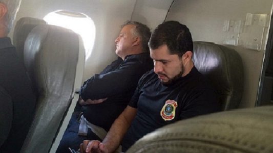 Carlinho Cachoeira é escoltado por agente da PF em voo. (Foto: Internet)