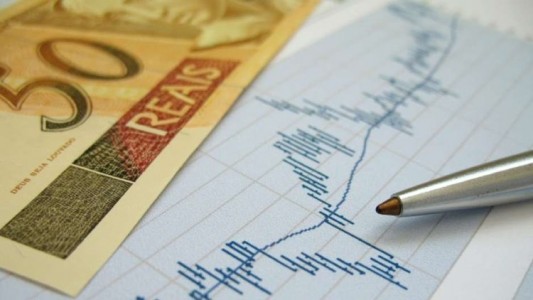 Stock market charts for investor analysis, with Brazilian Real $50 bills and pen, using selective focus on graph and pen.